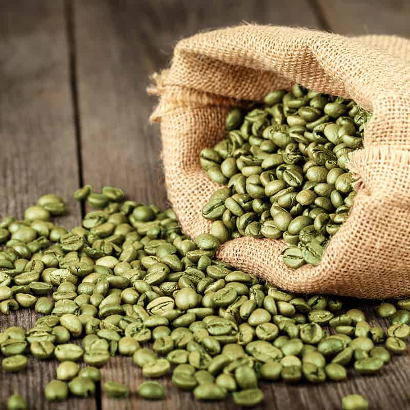 green coffee beans spilling from a burlap bag on wood