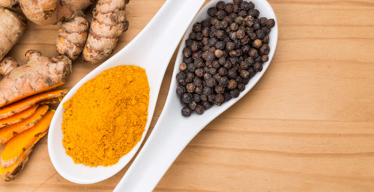 Spoons filled with turmeric and black pepper. Ginger on the ground.